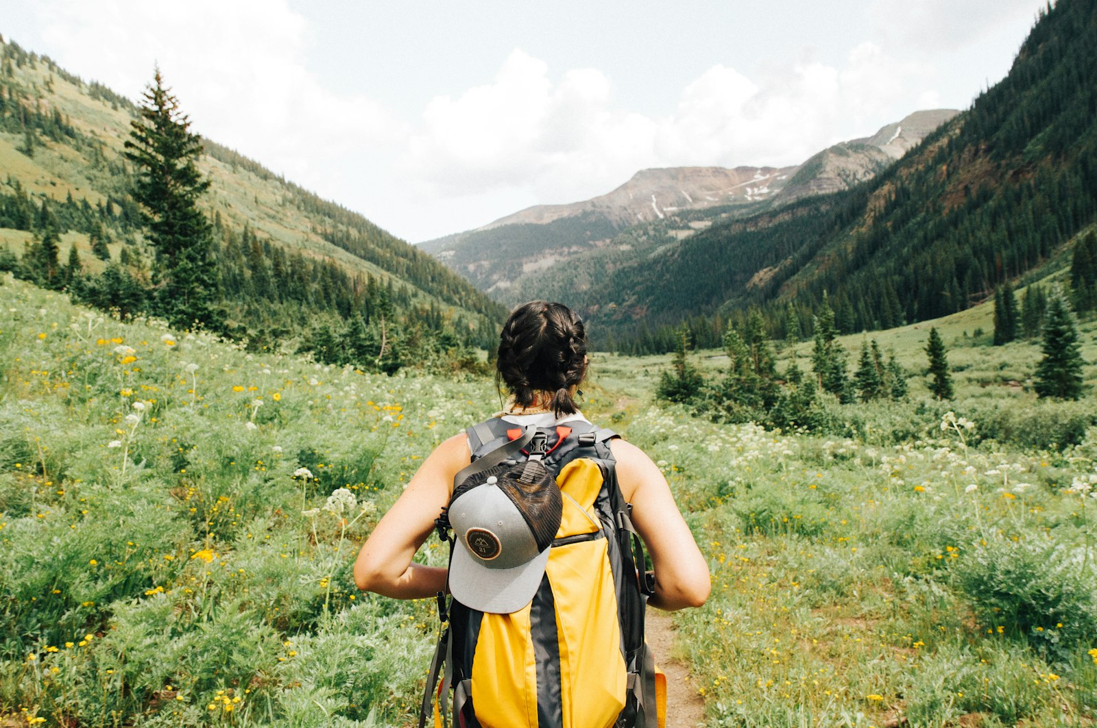 Two backpackers crossing a mountain meadow with packs on, snowy peaks in the distance.