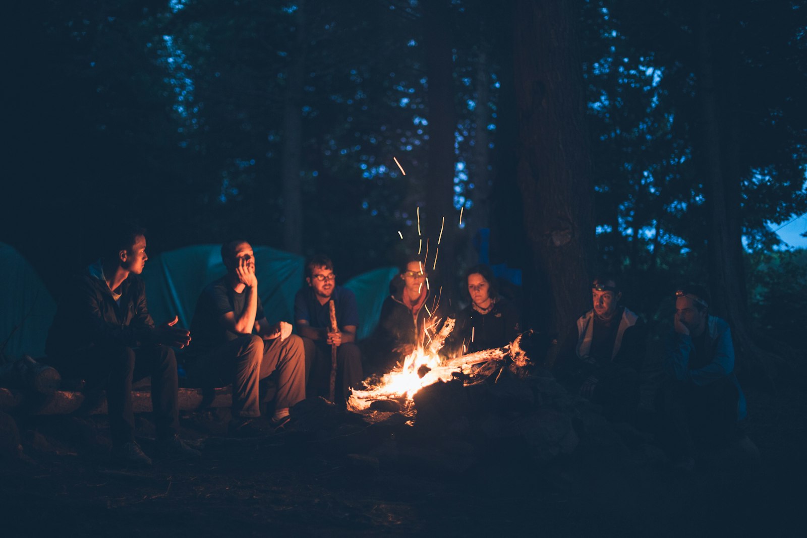 A small group of friends sitting around a campfire at dusk.
