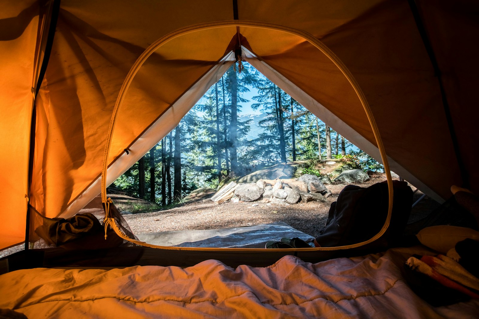 A small group campsite at golden hour, with two tents, a shared cooking area, and folding chairs around a fire ring.